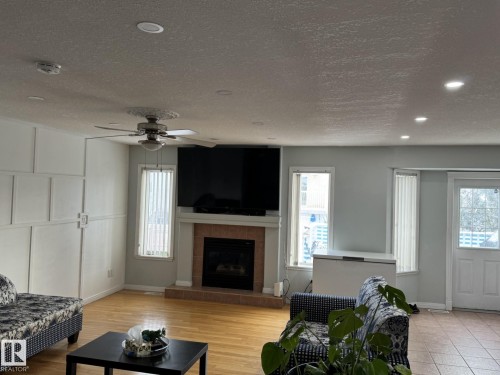 Living area featuring wood-finish flooring, a ceiling fan with light fixture, recessed lighting, and a fireplace with a tile hearth and mantel - 3139 34B Avenue, Edmonton, AB 