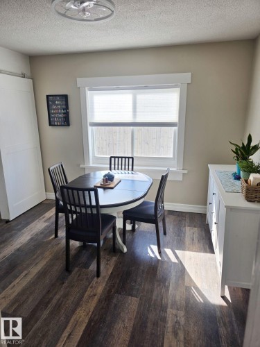 Dining area with dark wood-finish flooring, featuring a large window with white trim, a barn door, and a built-in white buffet cabinet with drawers. - 4825 52 Street, Elk Point, AB - Indoor Photo Showing Dining Room