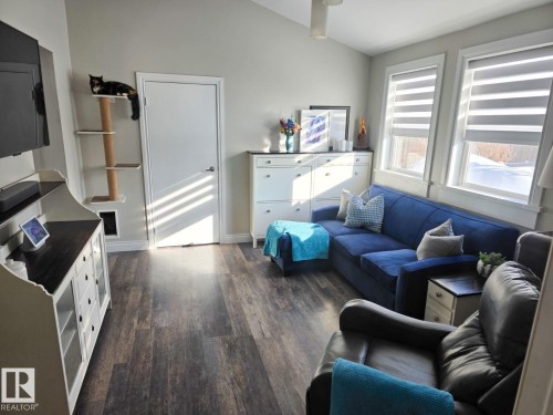 Living area featuring wood-finish flooring, multiple windows with zebra blinds, and vaulted ceilings. - 4825 52 Street, Elk Point, AB - Indoor Photo Showing Living Room