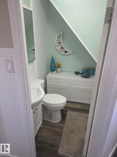 Bathroom featuring a white toilet, pedestal sink with vanity, and a mirror. - 4825 52 Street, Elk Point, AB - Indoor Photo Showing Bathroom