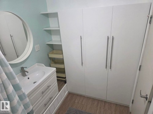 Bathroom featuring a modern vanity with integrated sink, a circular wall-mounted mirror, and a wall-mounted shelving unit. - 4825 52 Street, Elk Point, AB - Indoor Photo Showing Bathroom