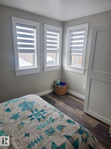 Room featuring three windows with white trim, wood-finish flooring, and a white interior door. - 4825 52 Street, Elk Point, AB - Indoor Photo Showing Bedroom