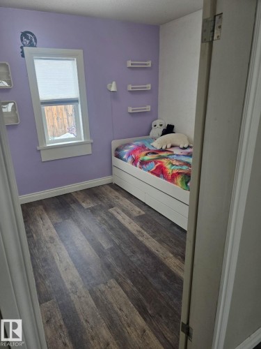 Room featuring wood-finish flooring, a single window with white trim, and light purple wall paint. - 4825 52 Street, Elk Point, AB - Indoor Photo Showing Bedroom