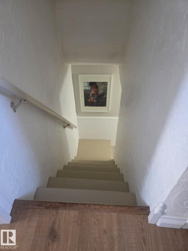 Wood-finish flooring at the top of the staircase with a white painted handrail - 4825 52 Street, Elk Point, AB - Indoor Photo Showing Other Room