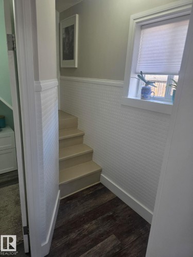 Staircase featuring wood-finish treads, textured wainscoting, and a window with a cellular shade - 4825 52 Street, Elk Point, AB - Indoor Photo Showing Other Room
