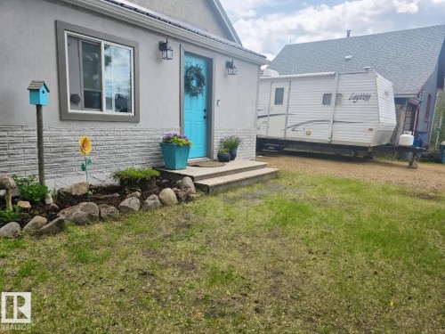 Front exterior featuring a vibrant blue entry door with a decorative wreath, two exterior sconces, and a window with gray trim. - 4825 52 Street, Elk Point, AB - Outdoor