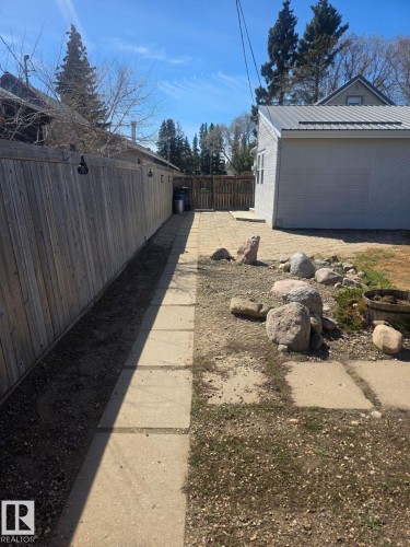 Rear yard featuring a wood privacy fence, concrete slab pathway, and a detached structure with a metal roof. - 4825 52 Street, Elk Point, AB - Outdoor