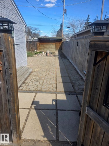 Gated entryway opening to a paved side yard featuring a decorative fence, a paver stone patio, and a separate concrete slab pathway. - 4825 52 Street, Elk Point, AB - Outdoor