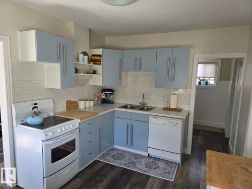 Kitchen featuring light blue cabinetry, white subway tile backsplash, and wood-finish flooring. - 4825 52 Street, Elk Point, AB - Indoor Photo Showing Kitchen With Double Sink