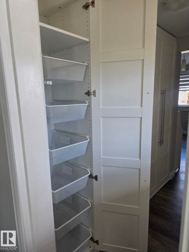 White pantry cabinetry featuring adjustable shelving and multiple pull-out wire baskets, complemented by wood-finish flooring. - 4825 52 Street, Elk Point, AB - Indoor