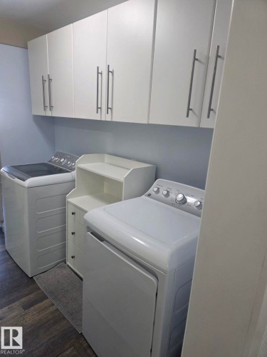 Laundry area with white overhead cabinetry, brushed nickel hardware, and wood-finish flooring. - 4825 52 Street, Elk Point, AB - Indoor Photo Showing Laundry Room