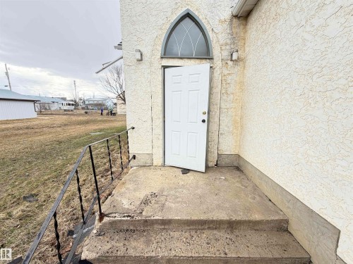 Stucco exterior featuring an arched transom window and concrete steps with a black metal railing - 5036 49 Street, Clyde, AB - Outdoor