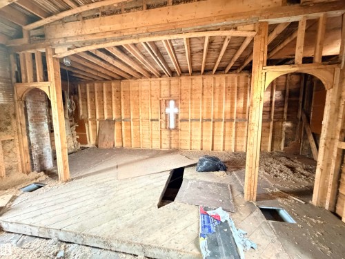 Exposed wood framing with an arched doorway, visible ceiling joists, and a partial brick wall - 5036 49 Street, Clyde, AB - Indoor