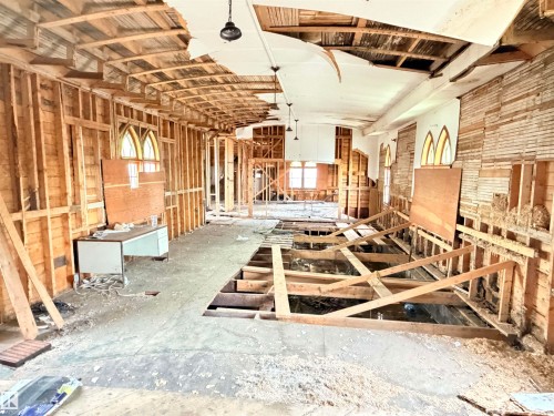 Interior space undergoing renovation, featuring exposed wood framing, arched windows, visible ceiling joists, partially removed flooring, and pendant light fixtures - 5036 49 Street, Clyde, AB - Indoor Photo Showing Other Room