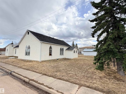 White stucco building with a dark shingle roof and gothic-arch windows - 5036 49 Street, Clyde, AB - Outdoor