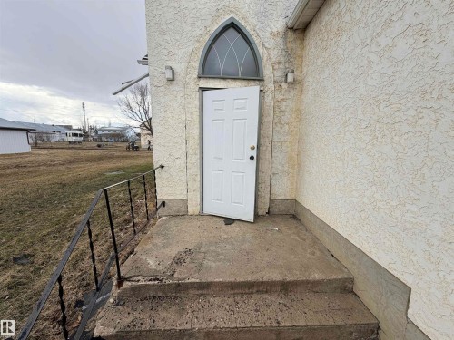 Stucco exterior with a white entry door featuring an arched transom window - 5036 49 Street, Clyde, AB - Outdoor