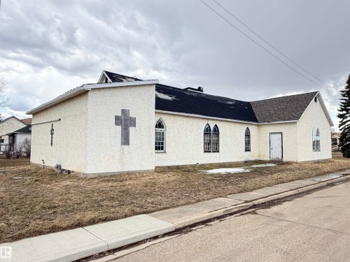 Stucco-clad structure featuring a multi-pitch shingle roof and multiple arched windows - 5036 49 Street, Clyde, AB - Outdoor With Exterior