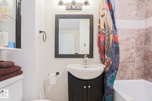 Bathroom featuring a vanity with a white basin and dark-finish cabinetry, a rectangular wall-mounted mirror, and a three-light vanity fixture - 5113 53 Avenue, Stony Plain, AB - Indoor Photo Showing Bathroom