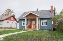 Charming bungalow with a blue stucco exterior, wood-shingle accents, and a covered front porch featuring a yellow entry door - 5113 53 Avenue, Stony Plain, AB  - Outdoor 