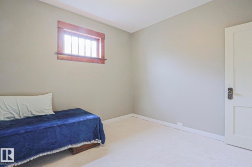 Neutral-toned walls and light-colored carpeting define this room, featuring a window with natural wood trim and multiple vertical muntins - 5113 53 Avenue, Stony Plain, AB - Indoor Photo Showing Bedroom
