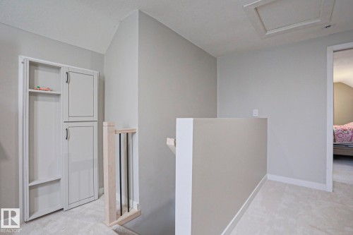 Built-in cabinetry with black hardware, light neutral wall paint, white baseboards, plush carpeting, and a wooden railing with black balusters - 5113 53 Avenue, Stony Plain, AB - Indoor Photo Showing Other Room