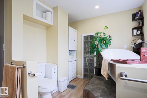 Soaking tub with integrated surround, glass block window, built-in shelving, wood-finish flooring, and recessed lighting - 5113 53 Avenue, Stony Plain, AB - Indoor