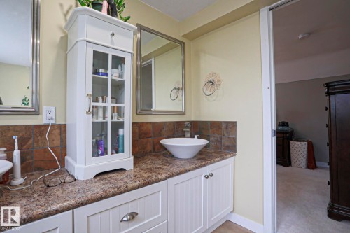 Bathroom vanity featuring a vessel sink, square tile backsplash, and white wood-finish cabinetry - 5113 53 Avenue, Stony Plain, AB - Indoor Photo Showing Bathroom
