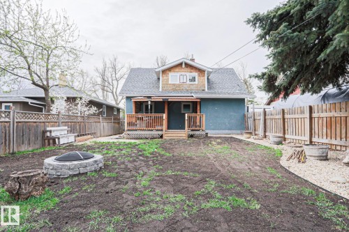 Rear exterior featuring a covered deck with wood railings, a stone-finished fire pit, mature perimeter trees, and a gravel-lined border - 5113 53 Avenue, Stony Plain, AB - Outdoor