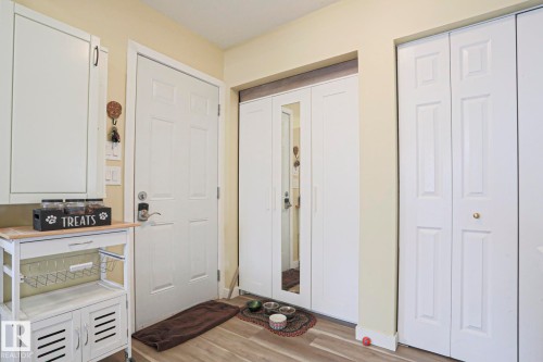 Entryway featuring wood-finish flooring, a white paneled door, and multiple storage closets with white bifold doors - 5113 53 Avenue, Stony Plain, AB - Indoor Photo Showing Other Room
