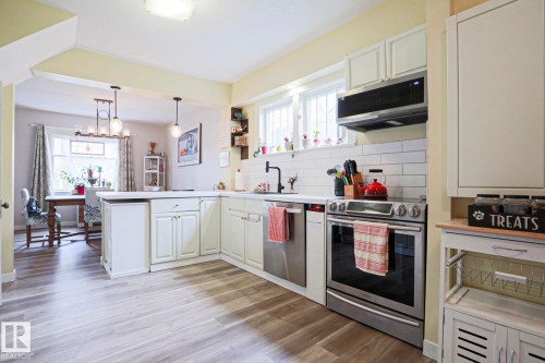 Kitchen featuring wood-finish flooring, white cabinetry, a subway tile backsplash, and stainless steel appliances - 5113 53 Avenue, Stony Plain, AB - Indoor Photo Showing Kitchen
