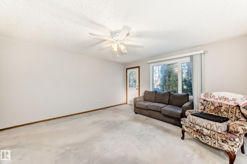 Spacious living area featuring light-colored carpeting, a ceiling fan with integrated lighting, a front entry door with decorative glass, and a large window with vertical blinds - 9716 162 Street, Edmonton, AB - Indoor