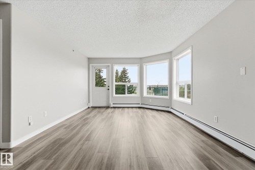 Spacious room featuring wood-finish flooring, light grey walls, and a textured white ceiling - 407 13635 34 Street Nw, Edmonton, AB - Indoor Photo Showing Other Room