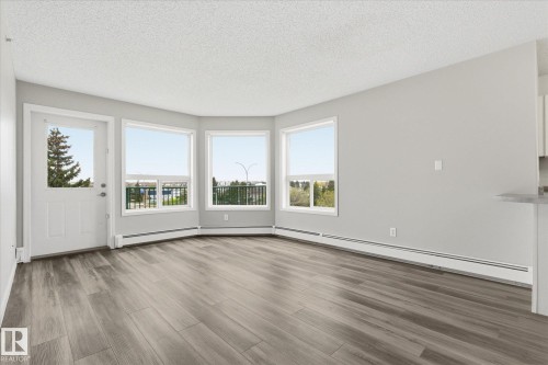 Spacious room featuring wood-finish flooring, light gray wall paint, and multiple windows - 407 13635 34 Street Nw, Edmonton, AB - Indoor