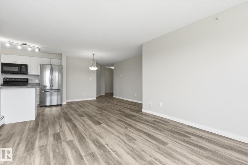 Open-concept living area featuring wood-finish flooring, light grey wall tones, and white trim - 407 13635 34 Street Nw, Edmonton, AB - Indoor Photo Showing Kitchen