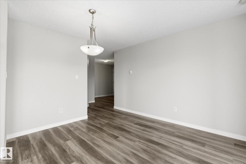 Spacious room featuring wood-finish flooring, light grey painted walls, white baseboards, and a textured ceiling - 407 13635 34 Street Nw, Edmonton, AB - Indoor Photo Showing Other Room