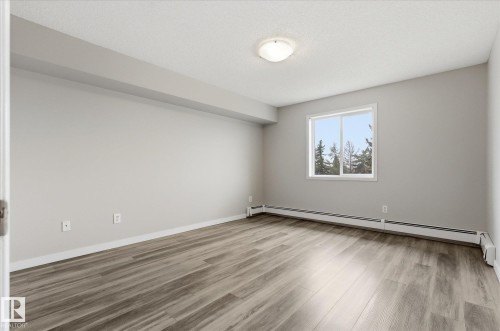 Spacious room featuring light gray walls, wood-finish flooring, and white trim - 407 13635 34 Street Nw, Edmonton, AB - Indoor Photo Showing Other Room