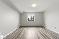 Spacious room featuring wood-finish flooring, a white window frame, and baseboard heating - 