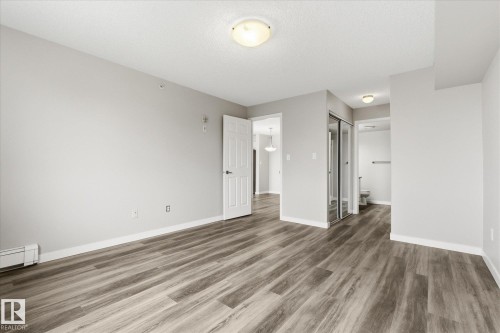 Spacious room featuring wood-finish flooring, light grey wall paint, and white baseboards - 407 13635 34 Street Nw, Edmonton, AB - Indoor Photo Showing Other Room
