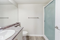 Bathroom featuring a white vanity with a built-in sink, stone-finish countertop, full-width mirror, a toilet, and a frosted glass shower enclosure - 