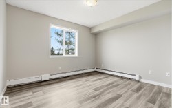 Spacious interior featuring wood-finish flooring, neutral wall tones, a large window, and baseboard heating - 
