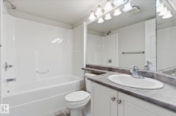 Full bathroom featuring a white tub and shower combination with chrome fixtures, a white toilet, and a vanity with white cabinetry, a gray countertop, and an integrated sink with a chrome faucet - 