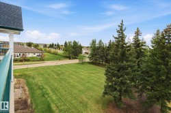 Expansive green space featuring a manicured lawn, perimeter fencing, mature evergreen trees, and distant residential structures - 