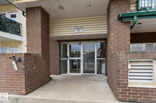Building entrance featuring a glass double door, brick columns, and a covered entryway with horizontal siding - 407 13635 34 Street Nw, Edmonton, AB - Outdoor With Exterior