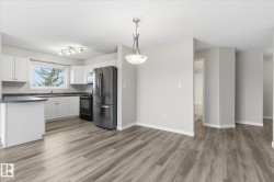 Open-concept kitchen and dining area featuring wood-finish flooring, white cabinetry, dark countertops, and stainless steel appliances - 