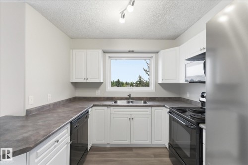 Kitchen featuring white cabinetry, dark countertops, and stainless steel appliances - 407 13635 34 Street Nw, Edmonton, AB - Indoor Photo Showing Kitchen With Double Sink