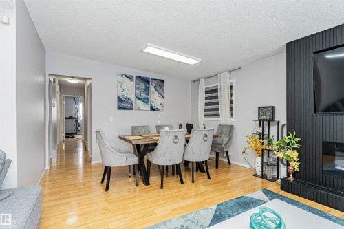 Open concept living and dining area featuring light wood-finish flooring, a contemporary fireplace with a fluted surround, and a rectangular window with horizontal blinds - 10412 39 Avenue, Edmonton, AB - Indoor Photo Showing Dining Room