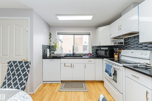 Bright kitchen featuring white cabinetry, black countertops, a patterned tile backsplash, wood-finish flooring, and a large window - 10412 39 Avenue, Edmonton, AB - Indoor Photo Showing Kitchen