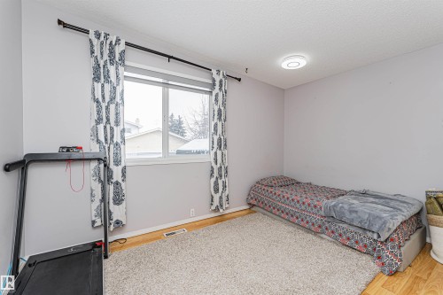 Room featuring wood-finish flooring, light grey painted walls, a large window with white trim, and a ceiling-mounted light fixture - 10412 39 Avenue, Edmonton, AB - Indoor Photo Showing Bedroom
