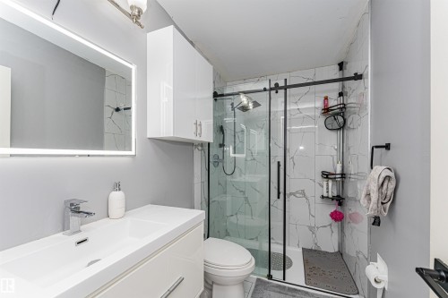 Bathroom featuring a floating white vanity with an integrated sink, a backlit rectangular mirror, and a glass-enclosed shower with black framing and white marble-look tile - 10412 39 Avenue, Edmonton, AB - Indoor Photo Showing Bathroom