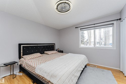 Bedroom featuring light gray walls, wood-finish flooring, and a large window with white trim - 10412 39 Avenue, Edmonton, AB - Indoor Photo Showing Bedroom